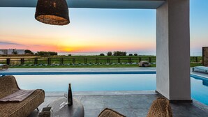 A poolside area with wicker furniture, a table with a glass, and a view of the sunset over the water. - Feyre Boutique Mansion-Echoes of the Sea by etouri (Rethymno)