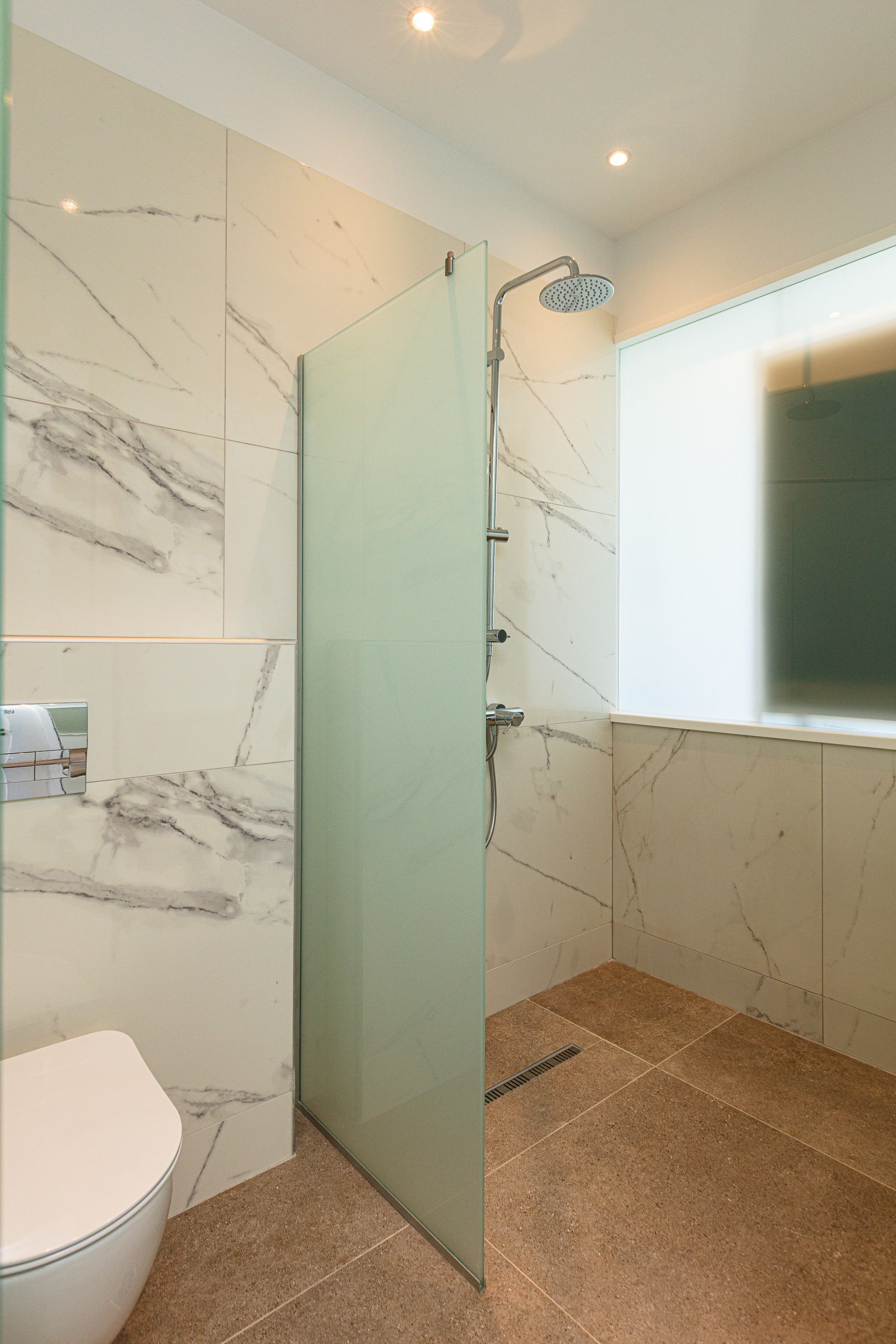 A modern bathroom with a glass shower enclosure, a toilet, and marble-patterned walls.