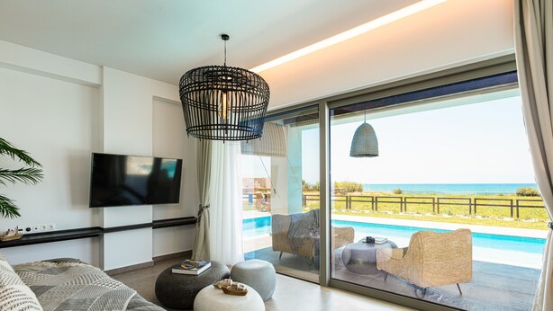 A modern living room with a large TV, comfortable seating, and a view of a pool and ocean. - Feyre Boutique Mansion-Echoes of the Sea by etouri (Rethymno)