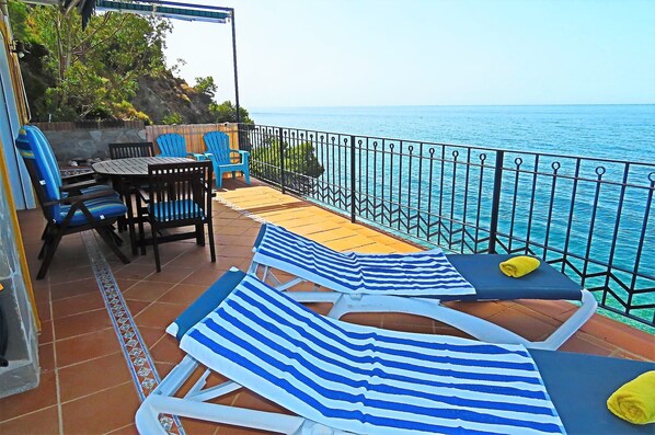 A terrace with a view of the sea, featuring lounge chairs, a table, and chairs.