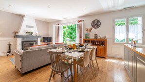 A modern kitchen with a dining area, a fireplace, and large windows.
