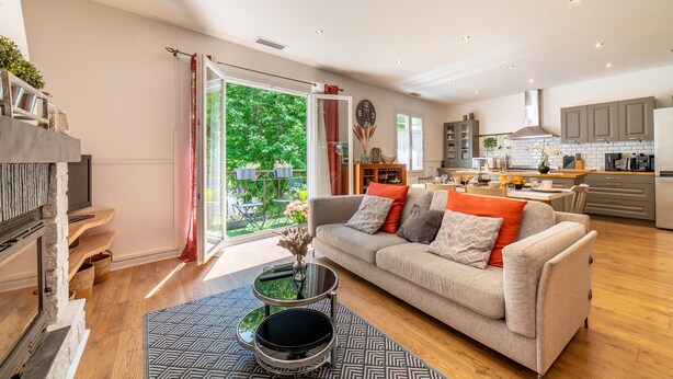 A modern living room with a sofa, coffee table, and a view of the kitchen and garden.