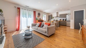 A modern living room with a sofa, coffee table, and a rug. The room has wooden flooring and a large window with curtains.