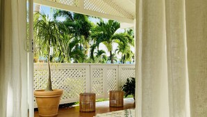 A covered patio area with a tiled floor, a large potted plant, and two wicker stools.