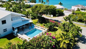 A residential area with a swimming pool, lush greenery, and a view of the ocean.