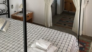Een slaapkamer met een bed, nachtkastje, spiegel en een raam met gordijnen.