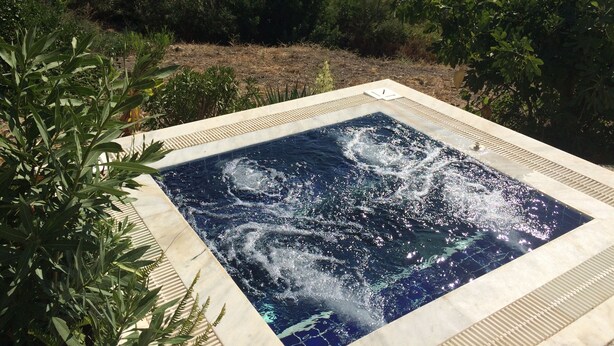 Een hottub omgeven door weelderige begroeiing en een bergachtige achtergrond.