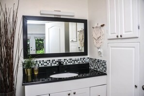 Un bagno con schienale rivestito in piastrelle bianche e nere, un lavandino bianco e uno specchio grande sopra.