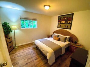 A bedroom with a bed, bedside tables, a lamp, a window, and a painting on the wall.