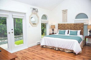 Una camera da letto con un letto grande, una testiera in legno, due abat-jour, uno specchio e vista su un giardino tramite una porta scorrevole.