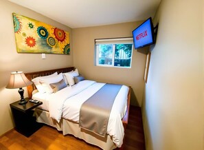 A hotel room with a bed, a nightstand, a lamp, a painting, a window, and a TV displaying Netflix.