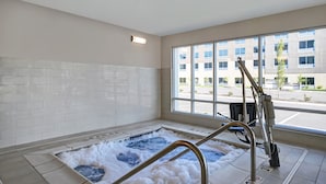 A spa area with a hot tub, a metal ladder, and a view of a parking lot through large windows.