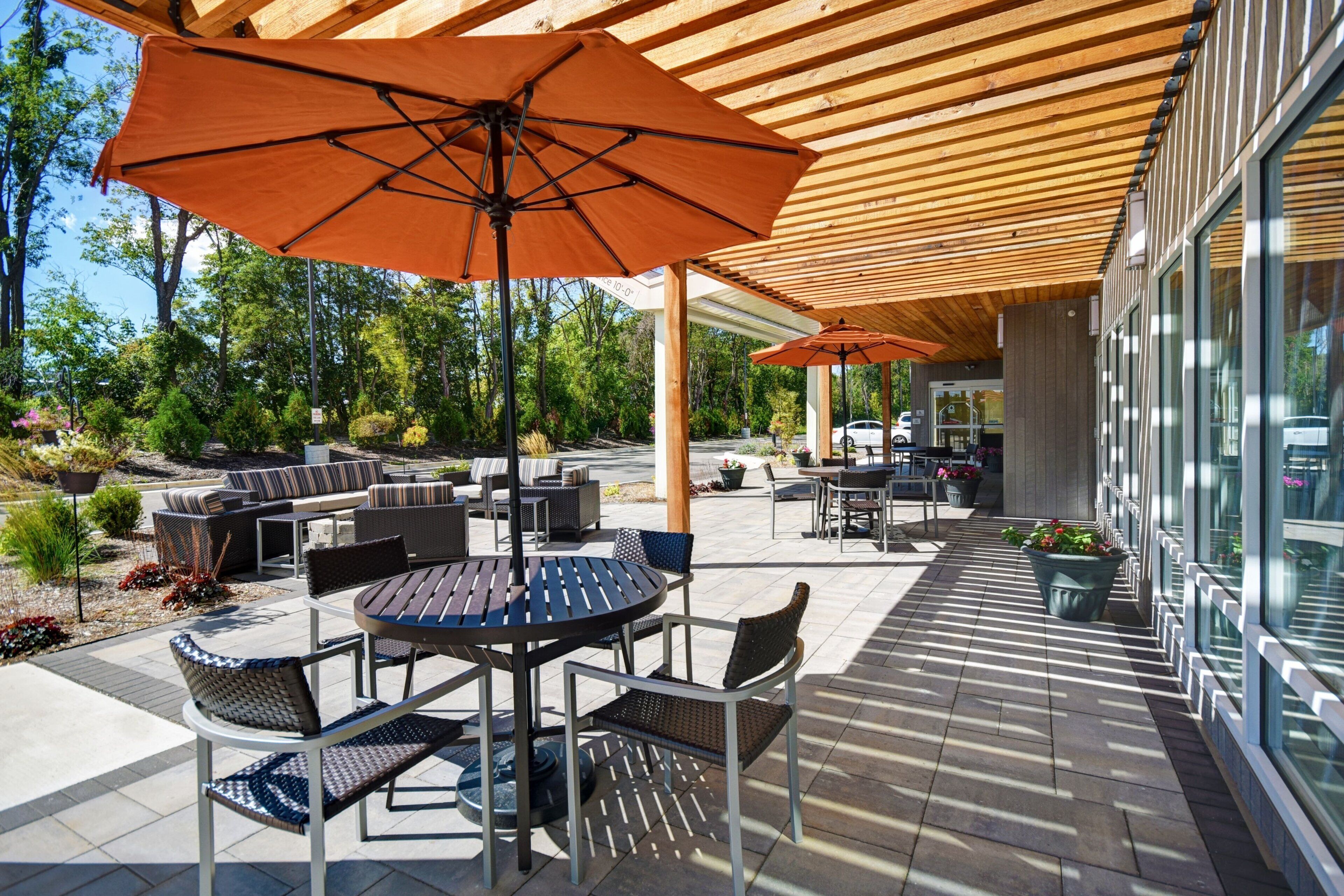 An outdoor patio area with round tables and chairs, large umbrellas, and a wooden pergola.