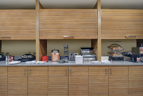 A buffet setup with wooden cabinets, a coffee maker, and various food items.