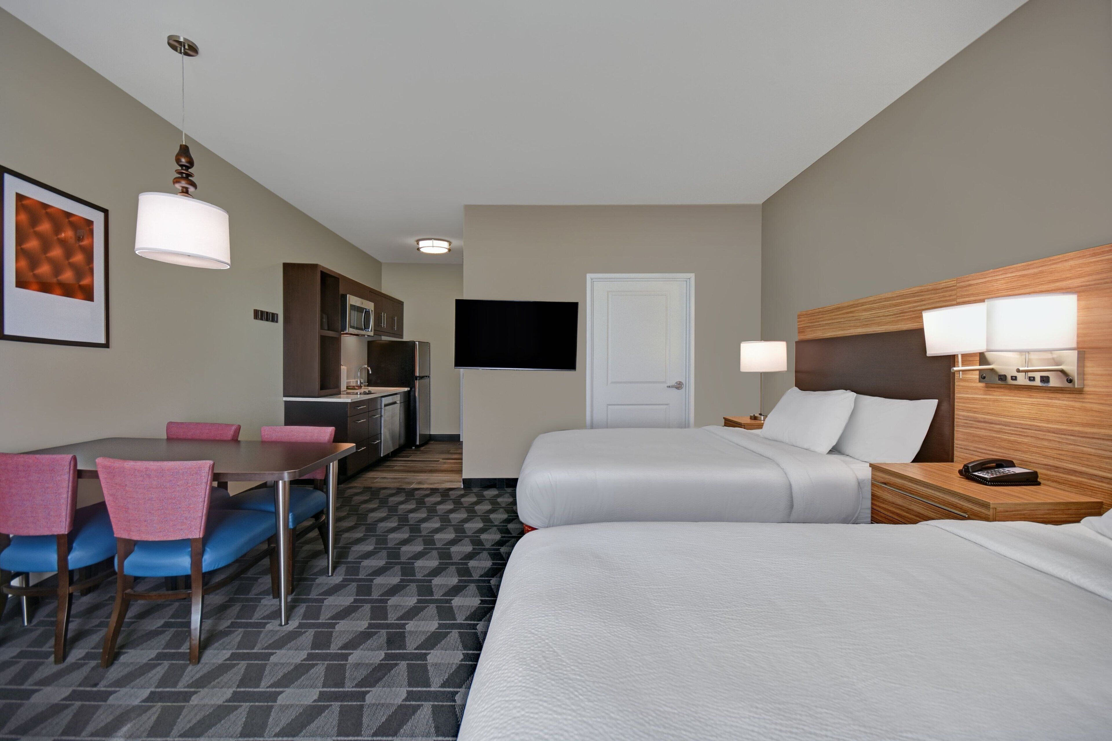 Une chambre d’hôtel avec deux lits, une table à manger avec des chaises, un coin cuisine et un téléviseur.