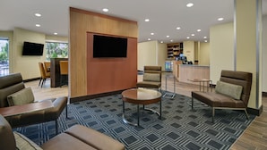A hotel lobby with seating areas, a television, a reception desk, and a minibar.