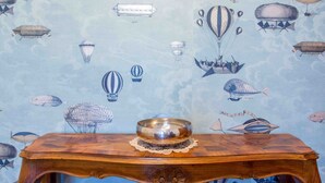 Una mesa de madera con un tazón de metal, frente a un papel tapiz con un diseño de cielo y nubes que incluye varios globos aerostáticos y dirigibles.