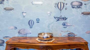A wooden table with a metal bowl on it, set against a wallpaper with a sky and cloud pattern featuring various hot air balloons and dirigibles.