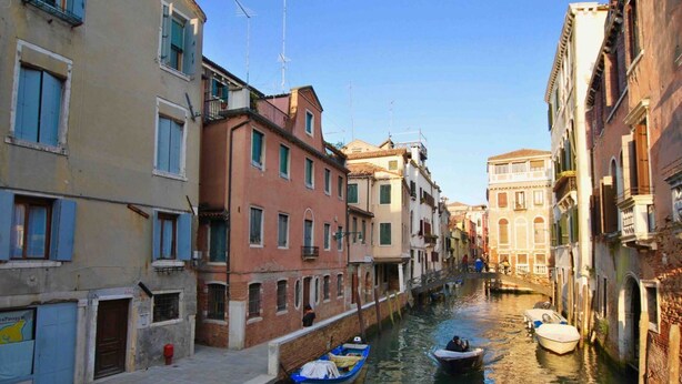 Un canal estrecho bordeado por edificios históricos con balcones y ventanas, y barcos amarrados a lo largo del agua.