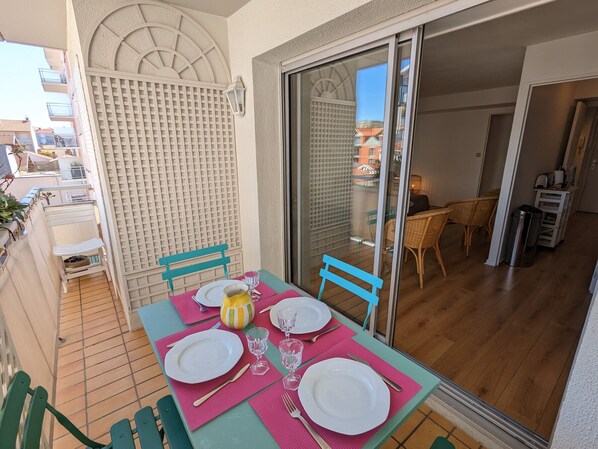 Ein Essbereich mit Tisch für zwei Personen, eine Schiebetür zu einem Balkon und Blick auf die umliegenden Gebäude.