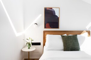 Una habitación de hotel con cama, una mesita de noche con un florero y una obra de arte colgada en la pared.