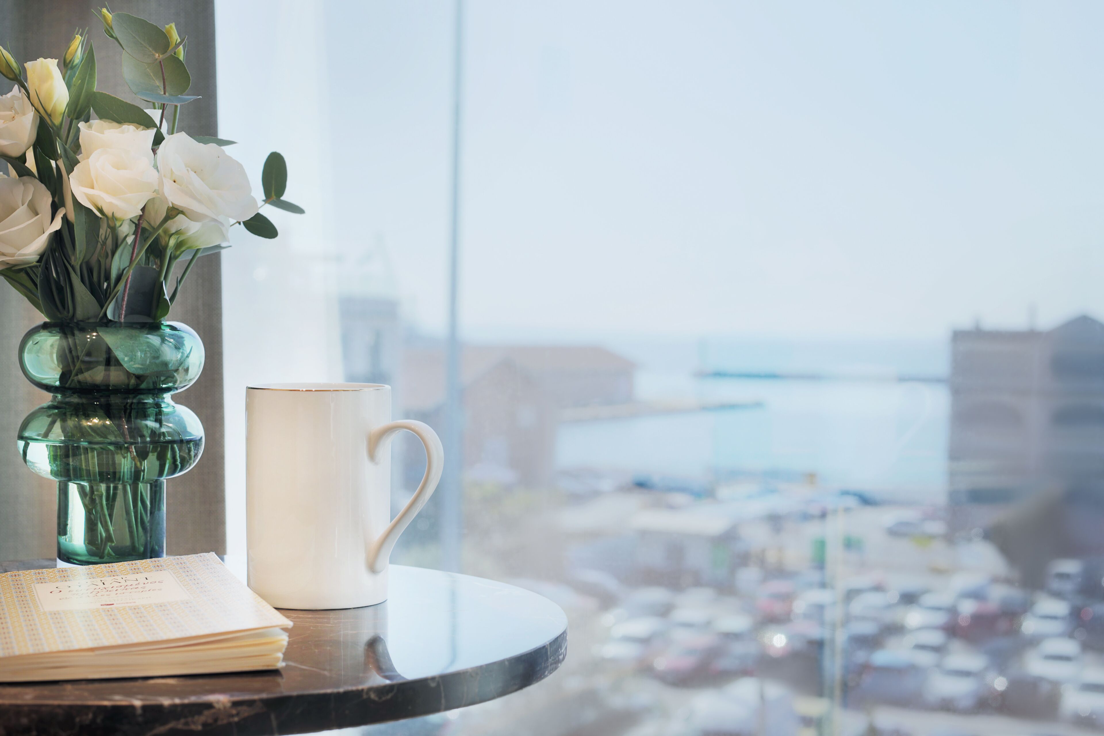 Une table avec un vase de fleurs blanches, une tasse blanche et un carnet.