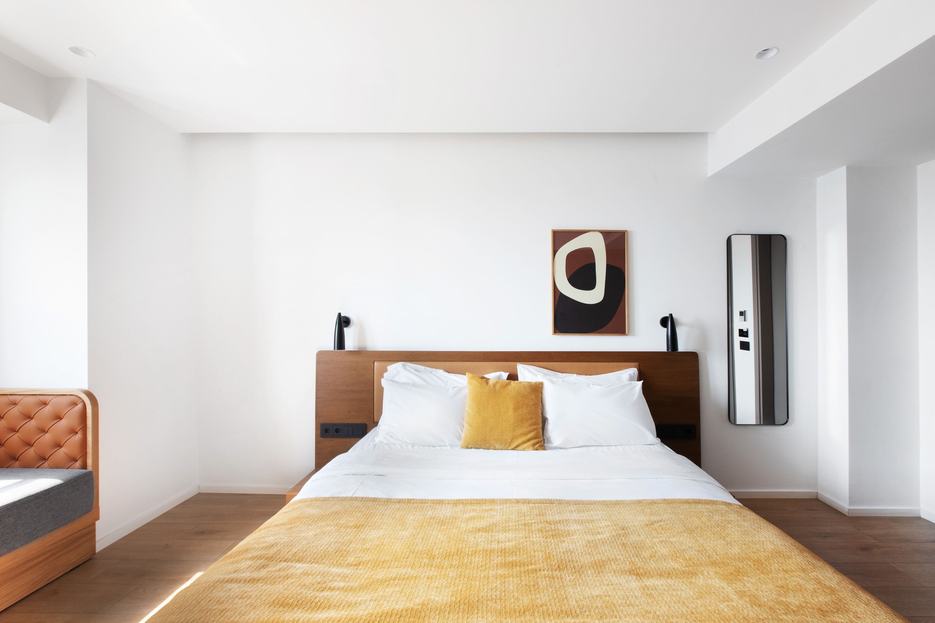 A modern hotel room with a large bed, a wooden headboard, a bedside table, and a nightstand.