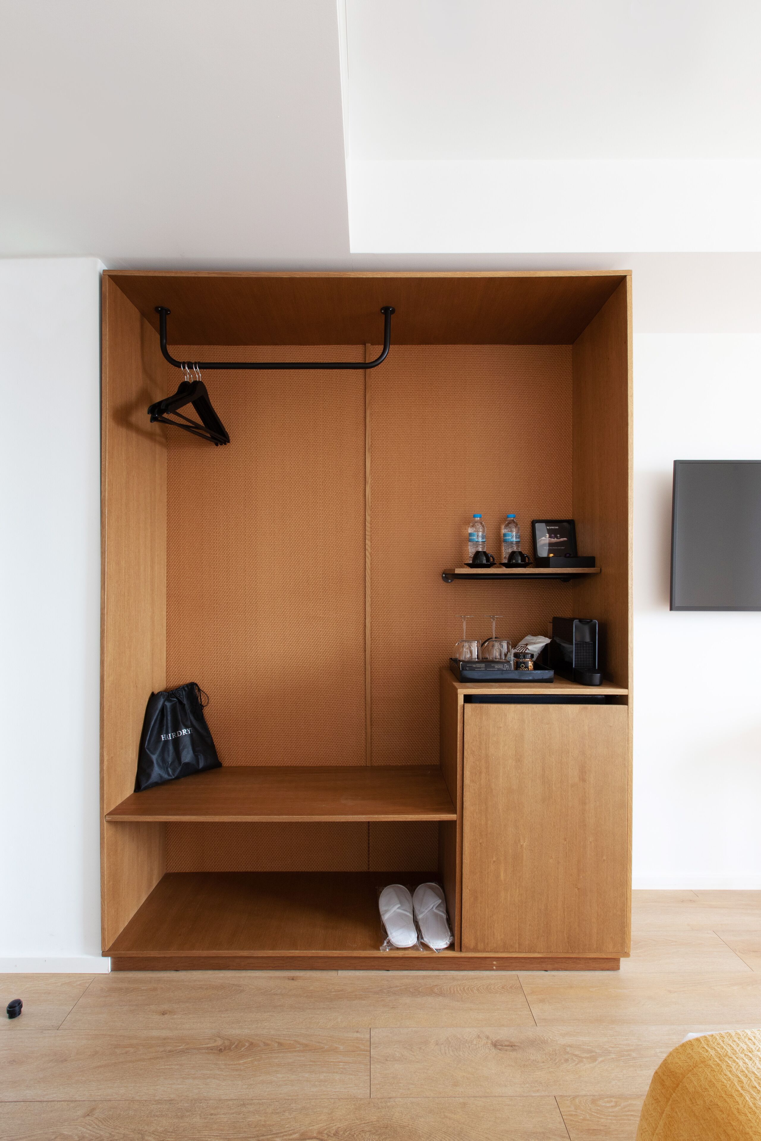 Una habitación compacta con un armario de madera, un escritorio pequeño con una computadora y un zapatero.