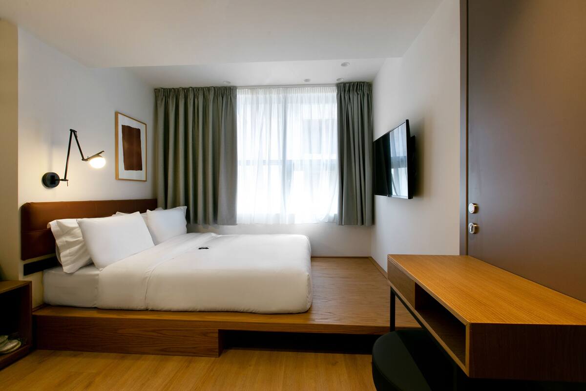A hotel room with a bed, a desk, a TV, and a window with curtains.