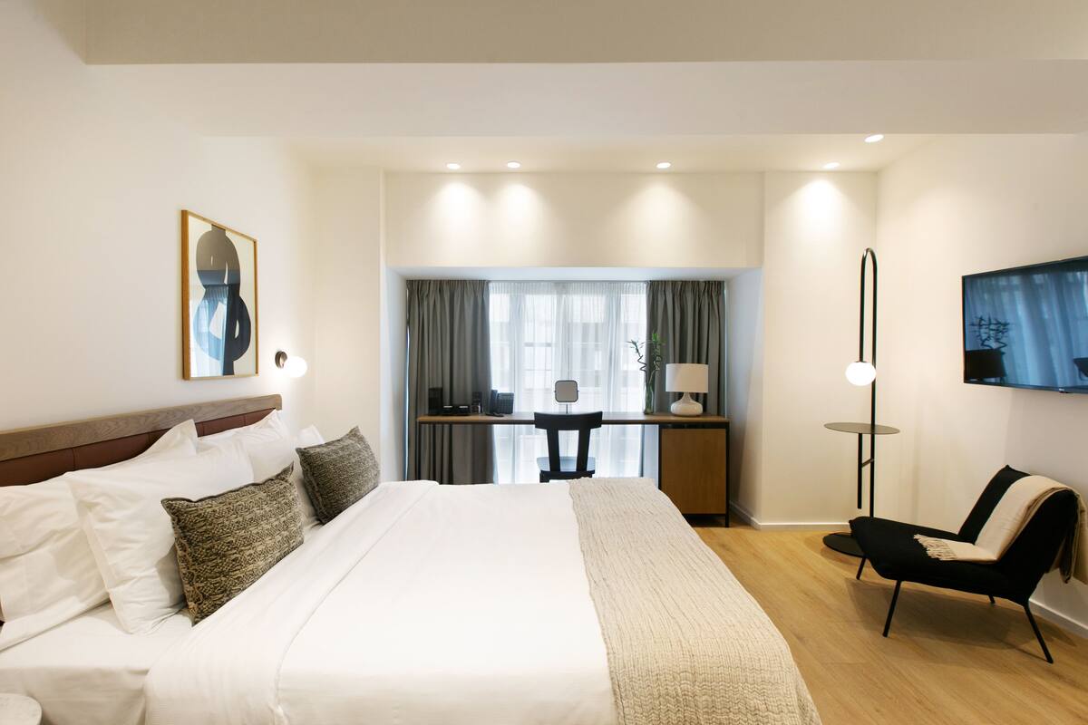 A hotel room with a large bed, a desk with a chair, a TV, and a lamp.