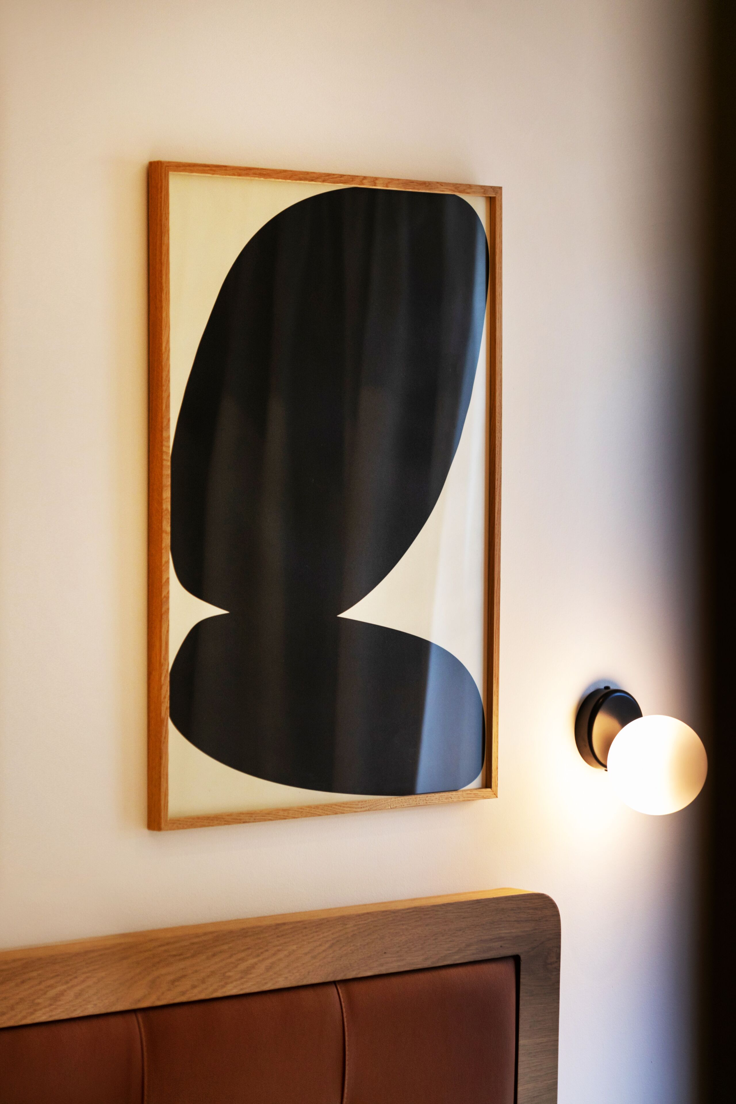 Un tableau abstrait encadré accroché au mur, un applique ronde et une tête de lit marron.
