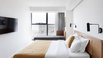 Habitación de hotel moderna con una cama grande, un televisor montado en la pared y vistas a la ciudad a través del ventanal.