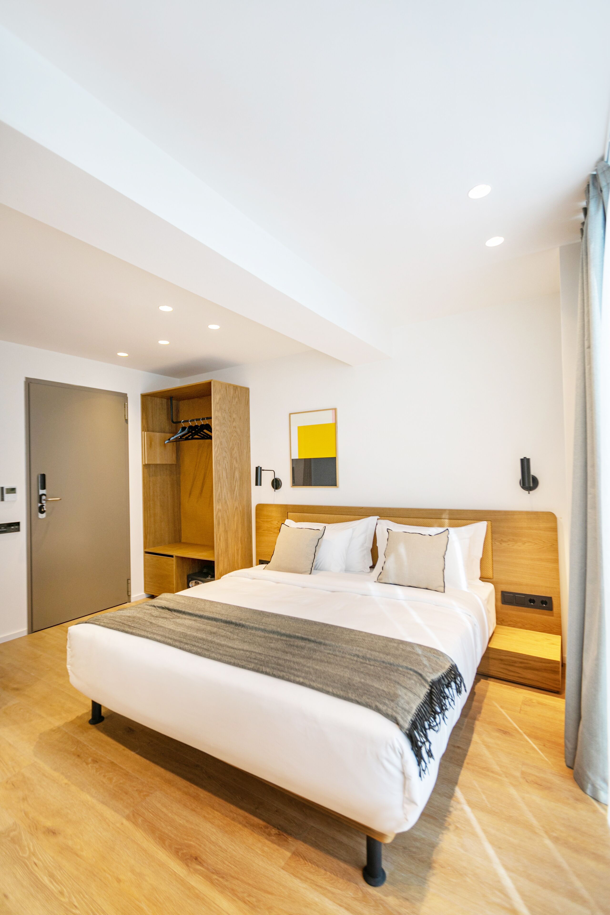 A modern hotel room with a large bed, wooden flooring, a built-in wardrobe, and a minimalist decor.