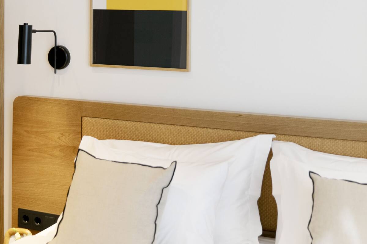A neatly made bed with white and beige pillows, a wooden headboard, and a modern abstract painting on the wall.