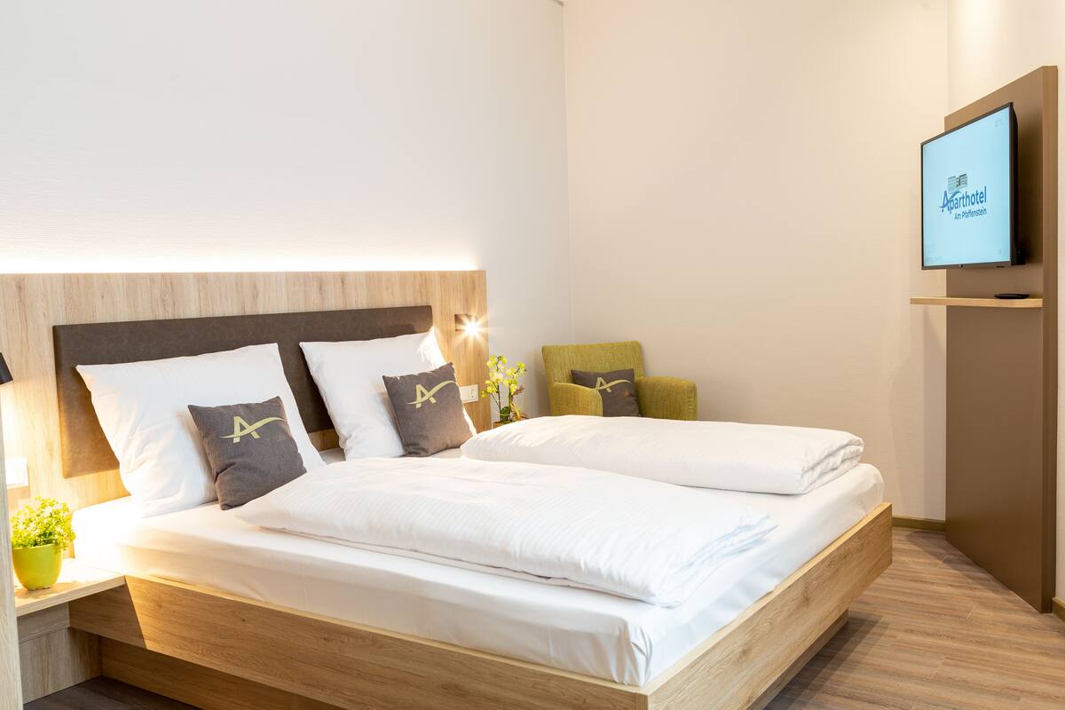 A modern hotel room with a large bed, a flat-screen TV mounted on the wall, and a wooden headboard.