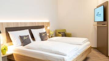 A modern hotel room with a large bed, a flat-screen TV mounted on the wall, and a wooden headboard.