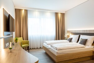 A hotel room with a wooden bed, a desk, a chair, a TV, and a window with curtains.