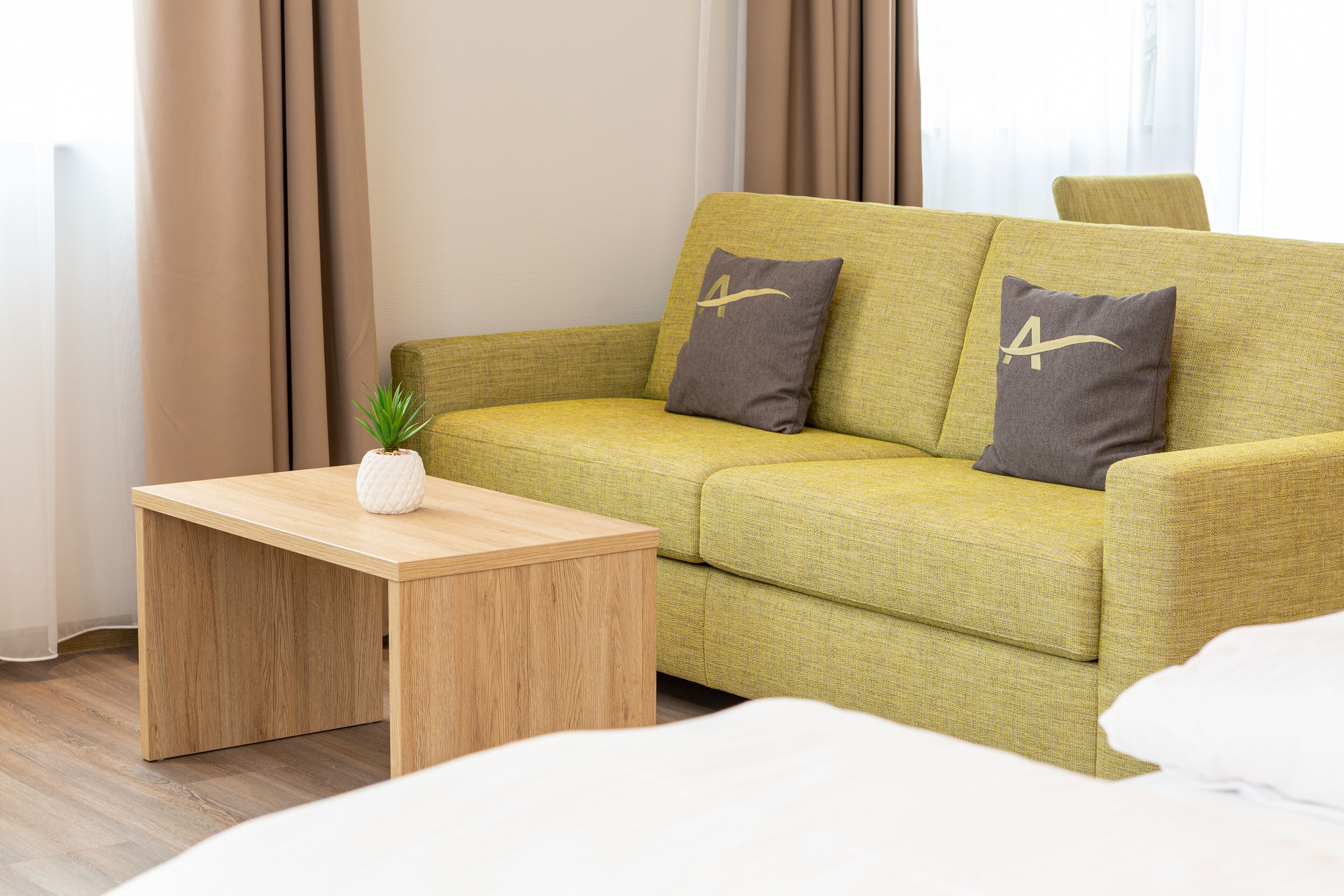 Ein grünes Sofa mit zwei Kissen, ein Holztisch und eine kleine Pflanze.