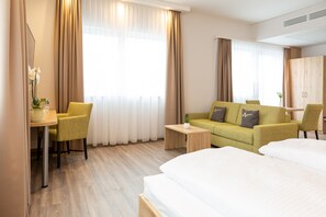 A hotel room with a bed, a sofa, a desk with a chair, and a small table. - Aparthotel Am Pfaffenstein (Klein-Winternheim)