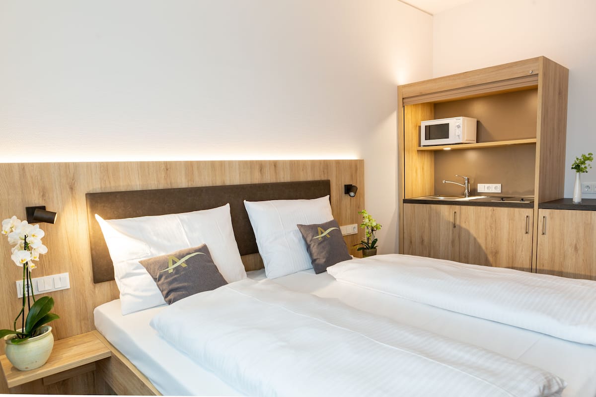 A double bed with white bedding and two pillows, a wooden headboard, a bedside table with a potted orchid, and a built-in microwave shelf.