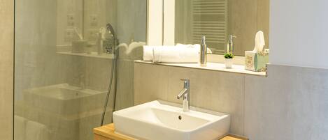 A modern bathroom with a glass-enclosed shower, a white sink, and a wooden vanity.