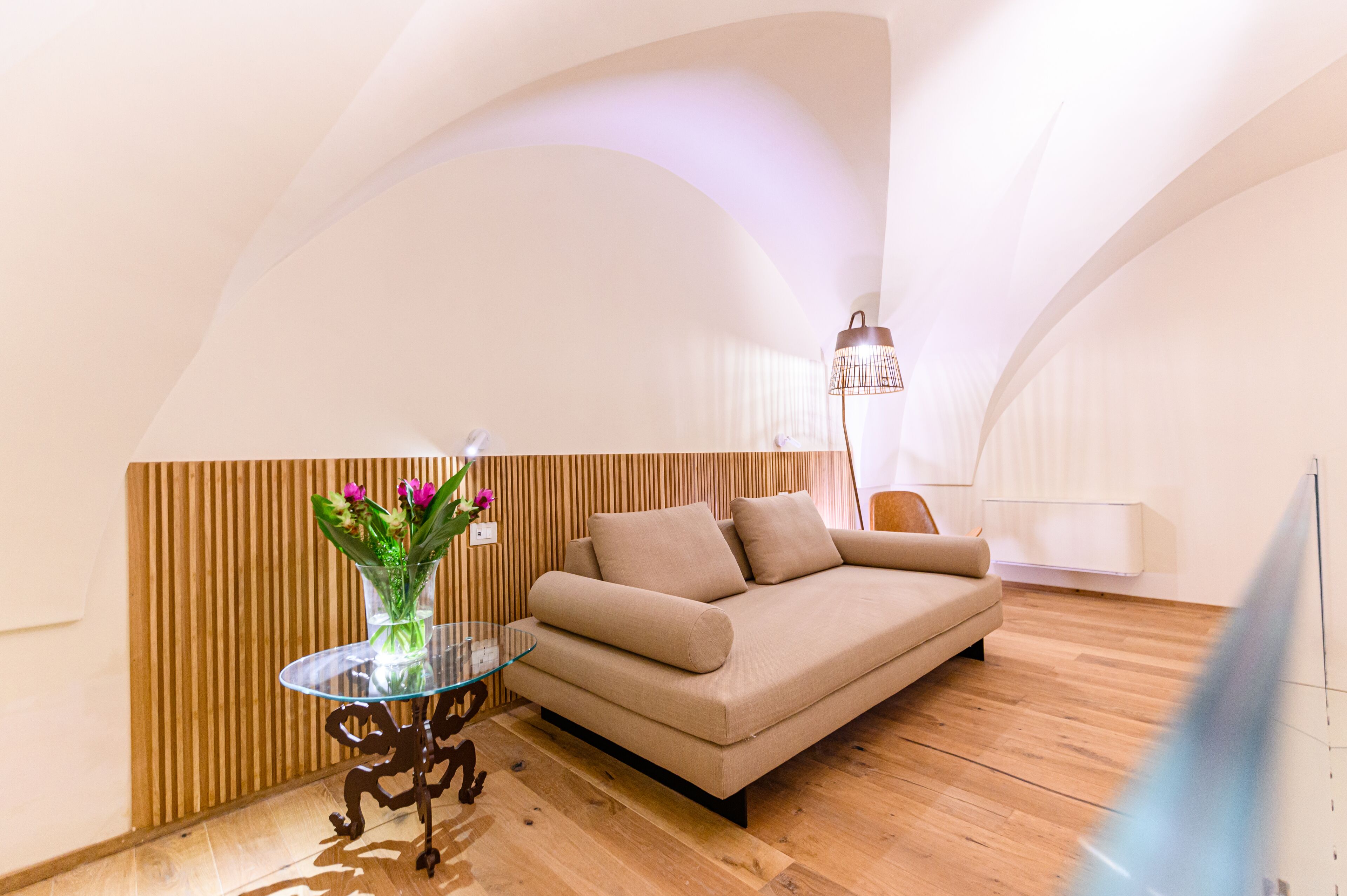 A modern living room with a sofa, a glass table with a vase of flowers, and a lamp.