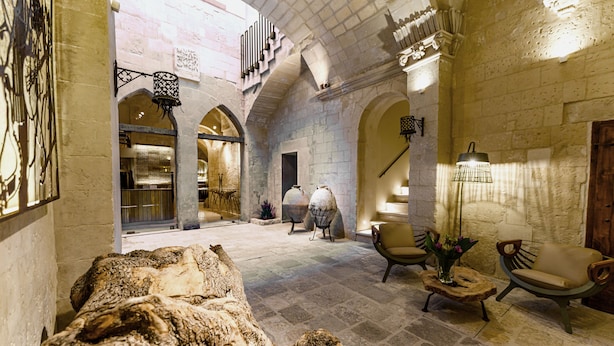 Un interior espacioso con paredes de piedra, arcos y una zona de estar central con una mesa de centro y sillas.