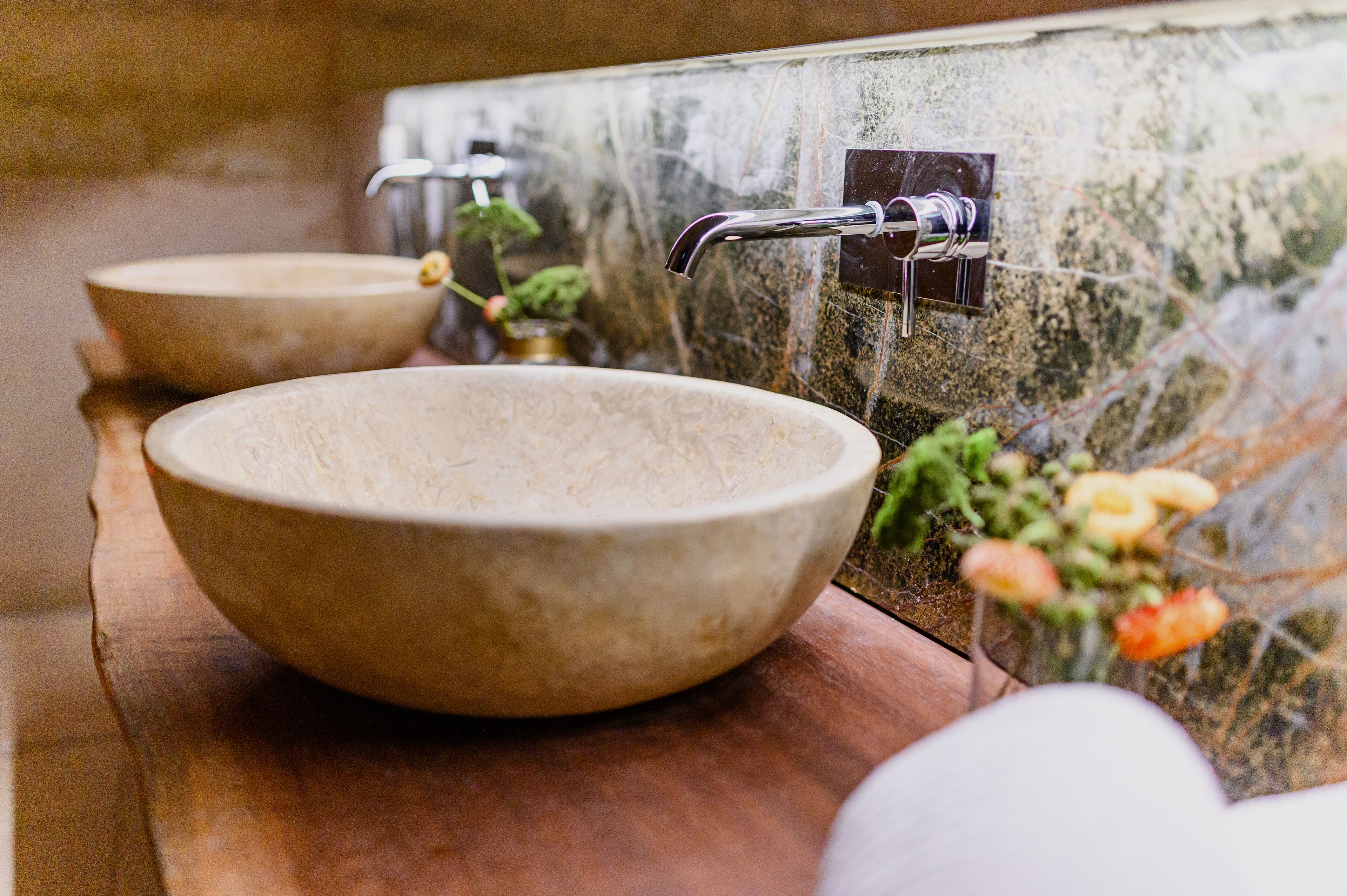 Two large, round, beige stone sinks with modern faucets on a wooden countertop.