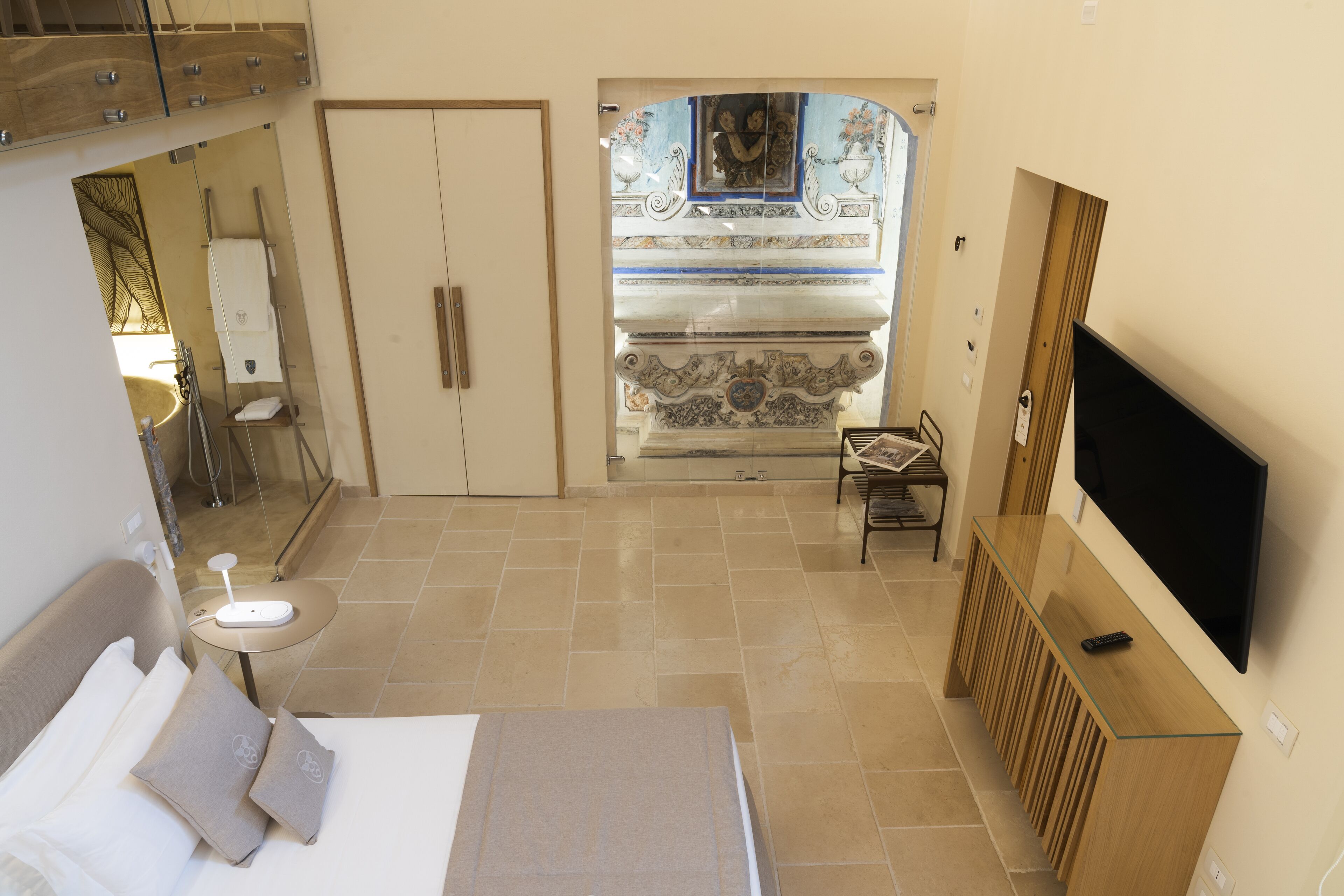 Habitación de hotel con cama, televisión, escritorio y baño visible a través de un arco.