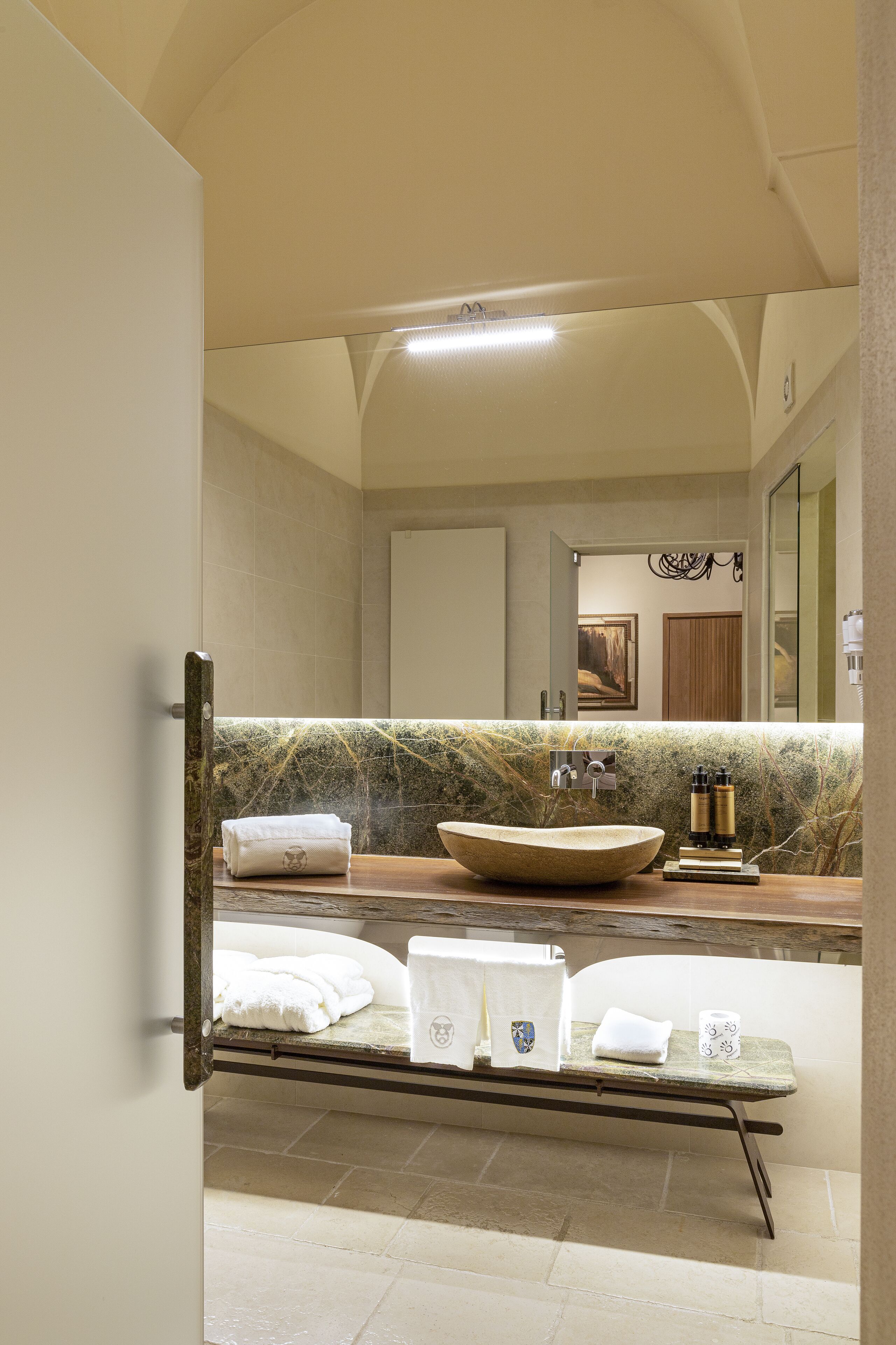 A modern bathroom with a large mirror, a marble countertop, a vessel sink, and neatly arranged towels.