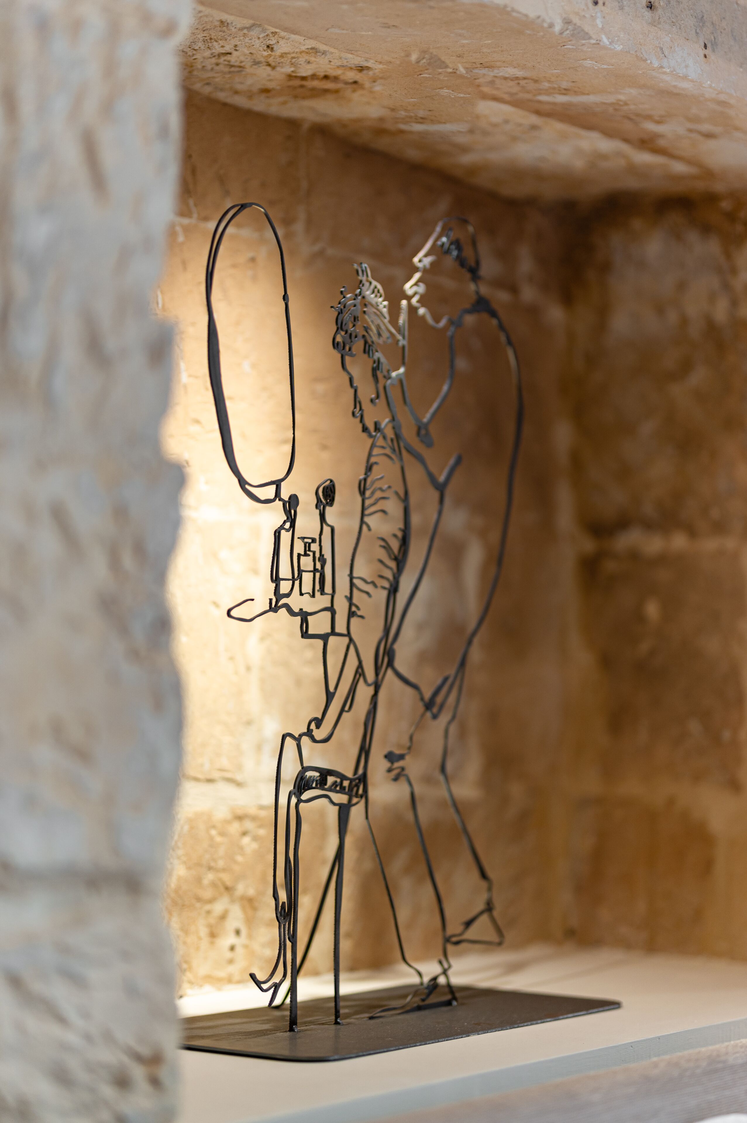Escultura metálica de una persona sosteniendo una cámara y otra persona en un entorno parecido a una cueva.