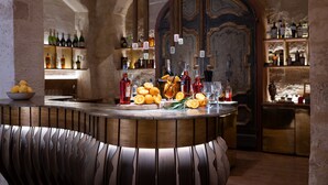 Una zona de bar con barra de madera, botellas, vasos y naranjas.