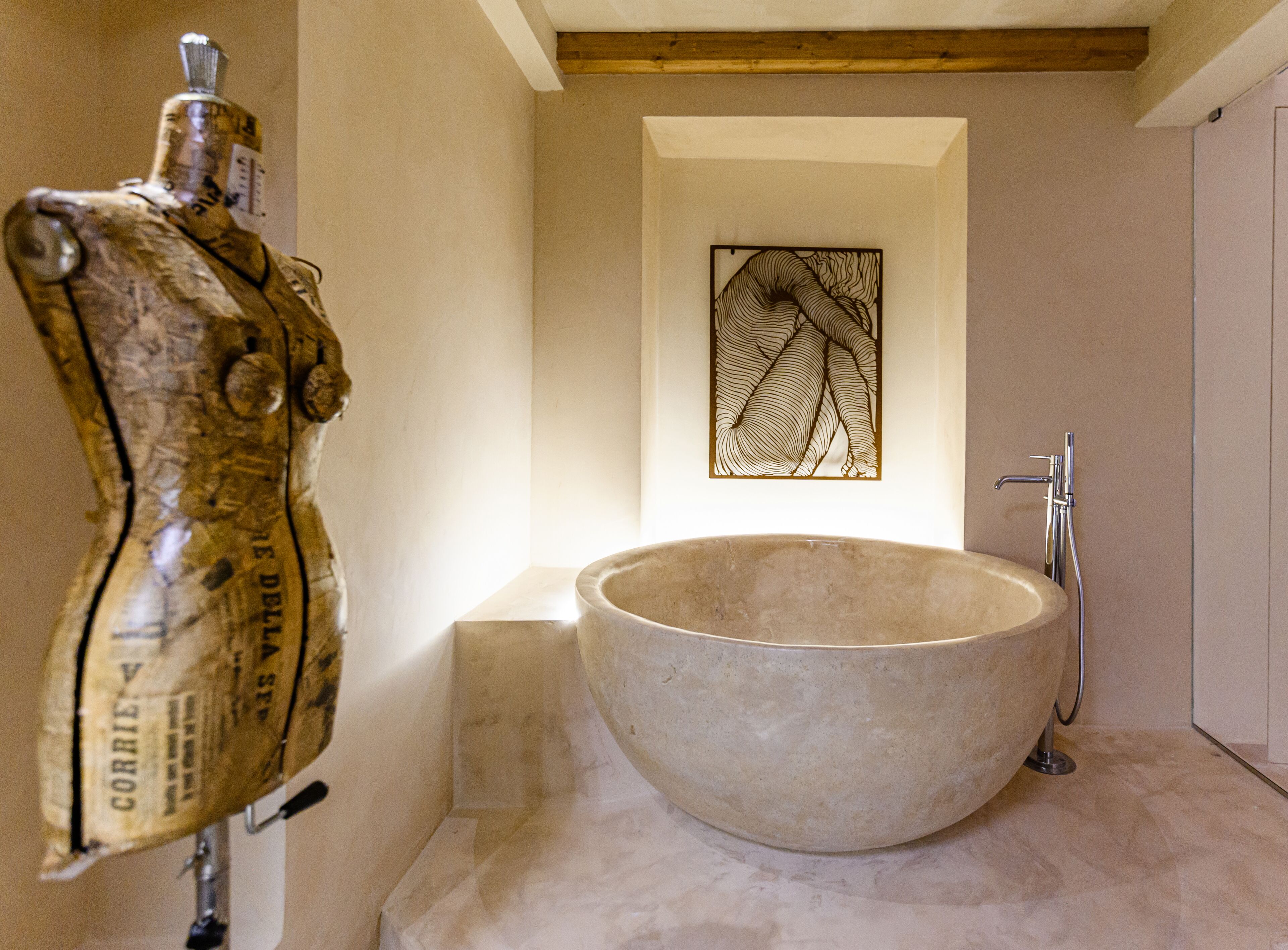 A bathroom with a large freestanding bathtub, a wooden ceiling, and a wall-mounted artwork.