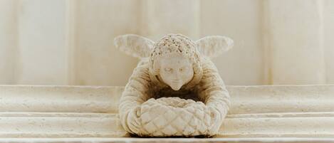 A sculpture of a figure with a textured head and hands, positioned on a stone ledge.